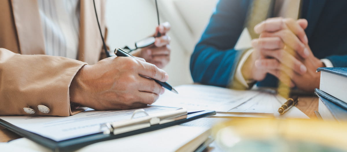 Close-up of two people reviewing documents at a desk, with clipboards and pens visible.