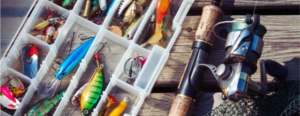 An open tackle box full of lures beside a rod and reel.