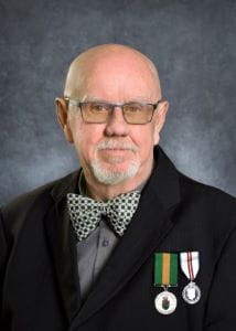 Wayne Cameron, wearing glasses, a black suit and bowtie. The Saskatchewan Volunteer Medal is pinned next to another medal on this jacket. 