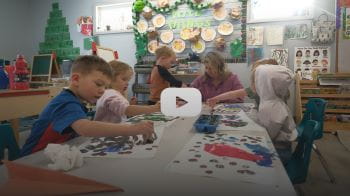 Children are sitting at a table painting. 