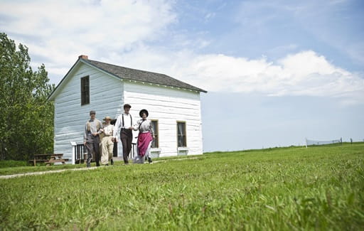 Four Park Interpreters historically dressed walk on grass at Cannington Manor Provincial Historic Park.