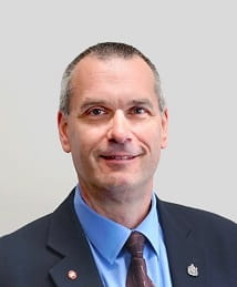 Deputy Minister Laurier Donais in a blue suit, light blue shirt and dark tie. 