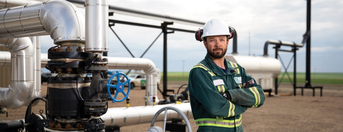 Man with arms crossed smiling at camera in working overalls and hard hat