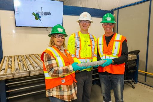 Minister Young a geologist and a government official examine a core sample in Nexgens core examination facility. Everyone in the photo is wearing Personal protective equipment with high visibility vests.
