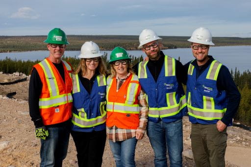 Minister Young with Nexgen officials standing on a burm overlooking Patterson lake. Everyone in the photo is wearing hardhats and Personal Protective equipment with high visibility vests.