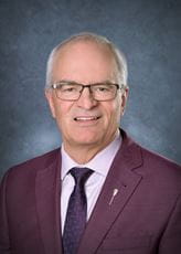 Mr. Blaine McLeod, MLA for Lumsden-Morse, wearing a dark maroon suit with a light pink shirt and dark tie with glasses on his face. 