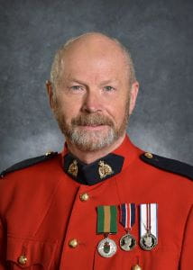 Dr. Bruce Neill, wearing a red RCMP jacket with the Saskatchewan Volunteer Medal pinned next to two other medals. 