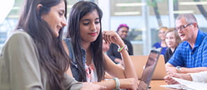 Two female students sitting at a table looking at a laptop in a common space at a university.