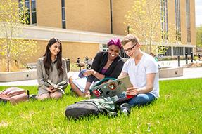 Students sitting on the lawn and smiling at each other