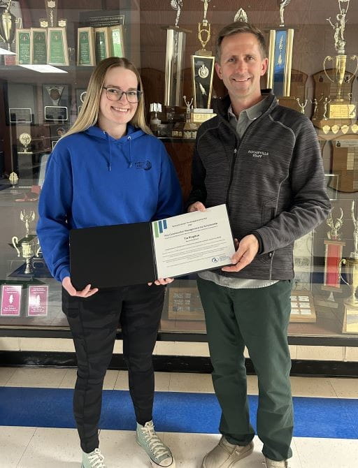Student receives SYA Industry Scholarship certificate in front of a trophy display.