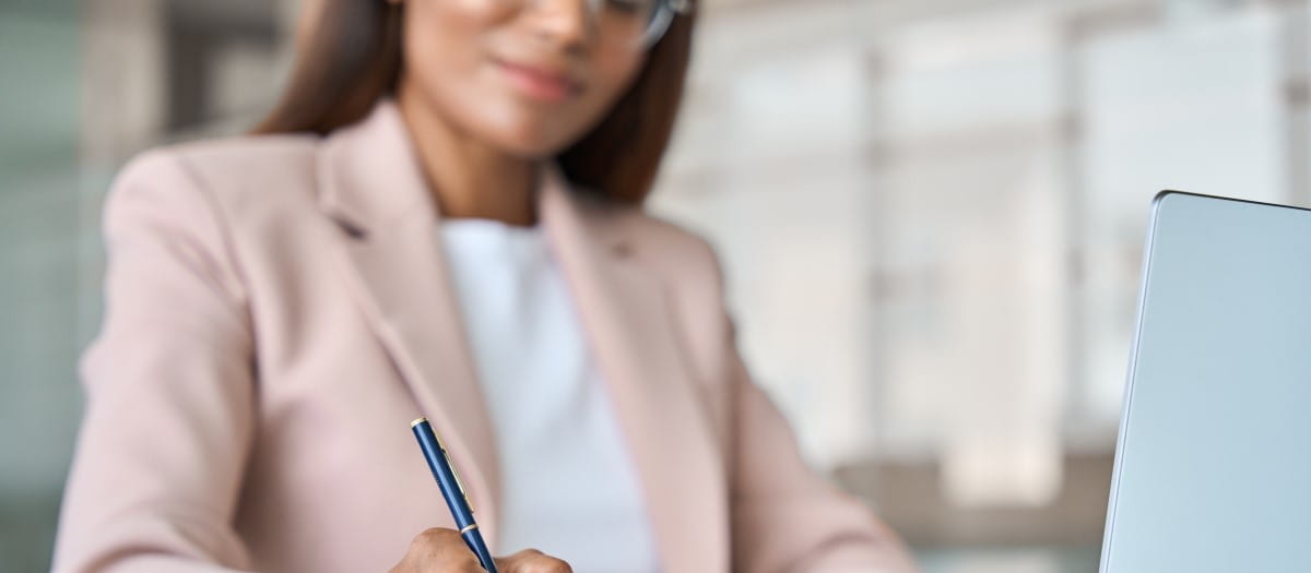 Close up of woman reviewing documents, with a notebook, pen and computer visible